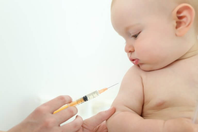 Bébé regarde une injection pendant que son bras est tenu pour être vacciné.