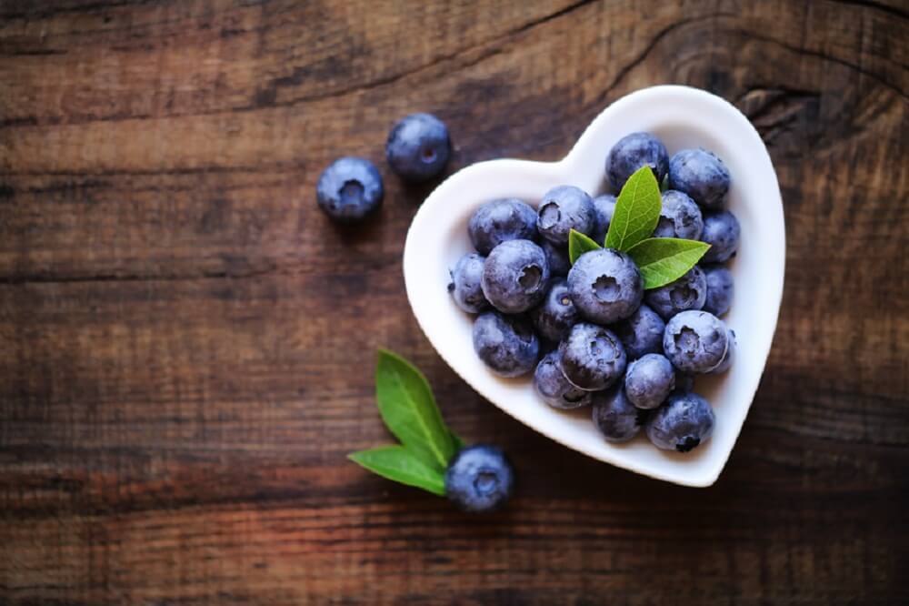 Fresh ripe garden blueberries in a white heart shape bowl on dark rustic wooden table. with copy space for your text